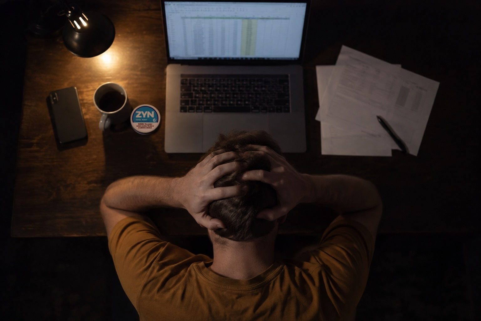 Stressed man at his desk at night, head in his hands, Zyn can beside the laptop